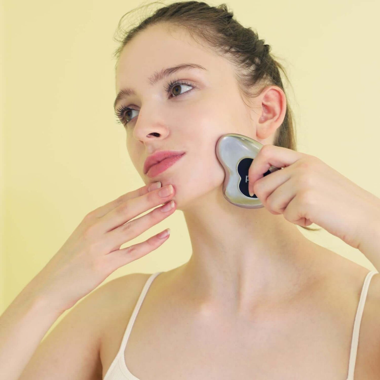 Woman using stainless steel cryo gua sha for facial massage to enhance skin and reduce puffiness.