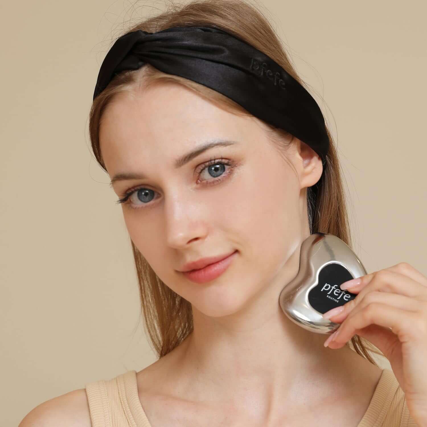 Woman showcasing Pfefe stainless steel cryo gua sha facial tool with a black headband for skincare.